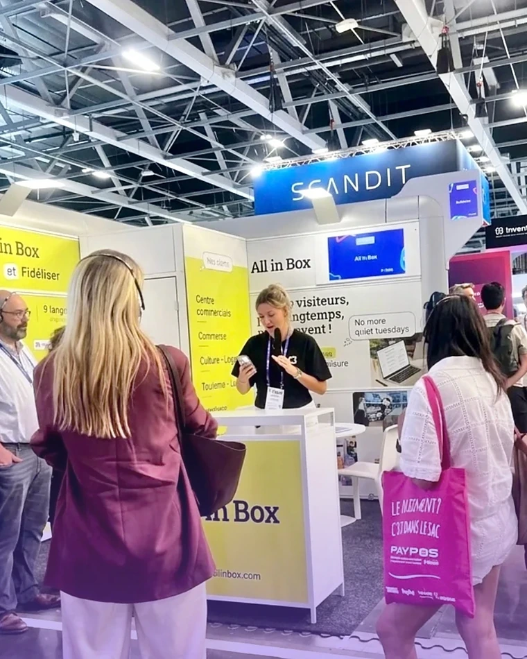 Une conseillère All in Box présente la plateforme à des visiteurs sur le stand de la NRF Europe 2026