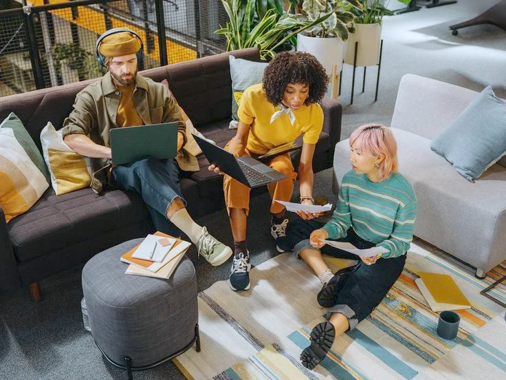 Trois personnes réunies autour de leurs ordinateurs et de documents papier dans un espace de travail aux couleurs chaleureuses