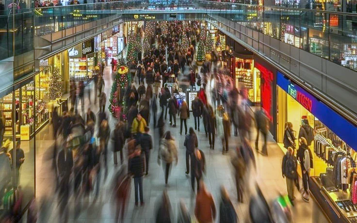 Vue plongeante sur la galerie d’un centre commercial en soirée, les passants en mouvement devant les vitrines éclairées