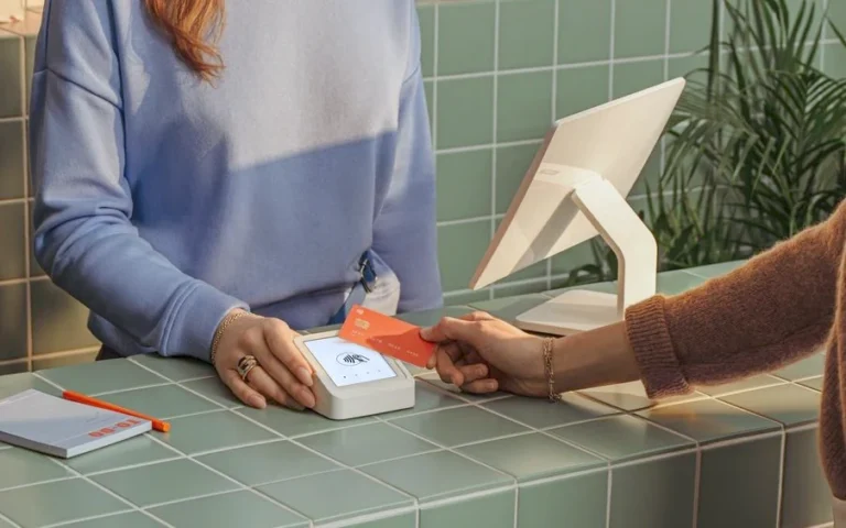 Au comptoir carrelé de vert d’une boutique, une cliente approche sa carte bancaire d’un terminal de paiement tenu par la commerçante