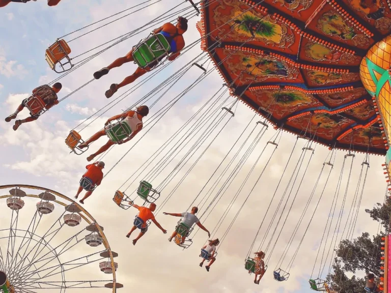 Chaises volantes et grande roue d’un parc de loisirs vues en contre-plongée au coucher du soleil