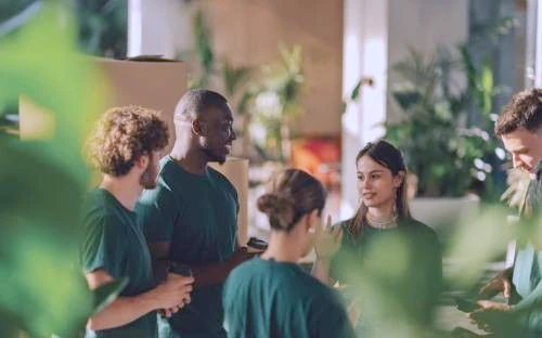 Un groupe de personnes en tee-shirts verts discutent debout dans un espace de travail entouré de plantes