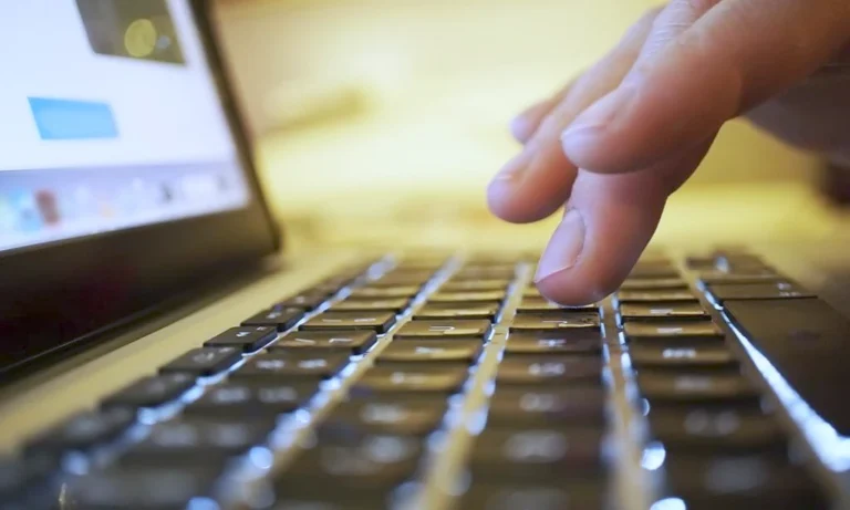 Gros plan sur un doigt qui s’apprête à appuyer sur une touche du clavier d’un ordinateur portable, l’écran affichant une interface en arrière-plan